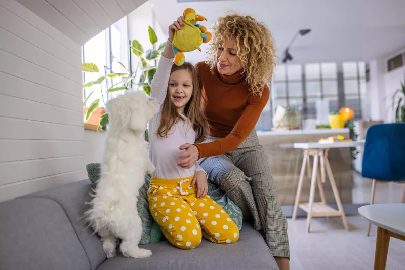 Cheerful mother and her daughter playing with Maltese