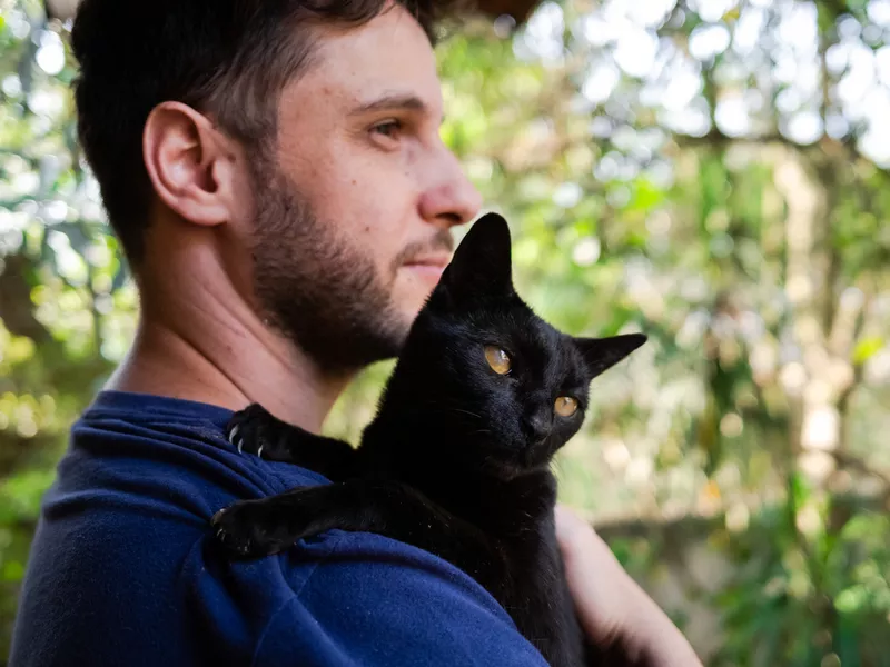 Man holding a cute black cat on his shoulder