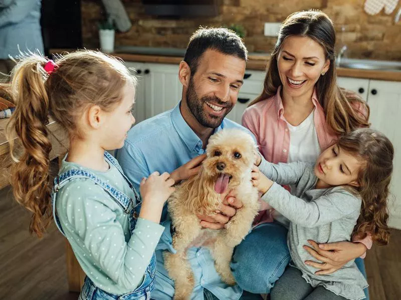 Happy parents and their daughters having fun with a dog at home.